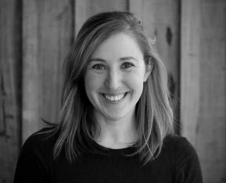 Portrait of a smiling woman with long hair against a wooden background.