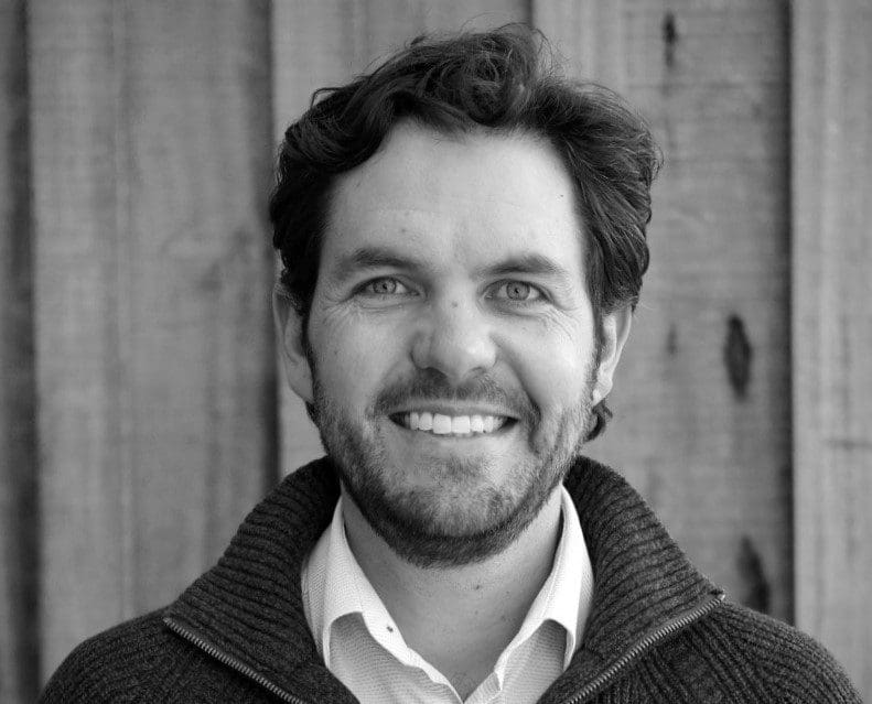 Smiling man with beard in casual sweater against wooden background.
