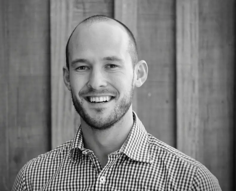 Smiling bald man in checkered shirt against wooden background.