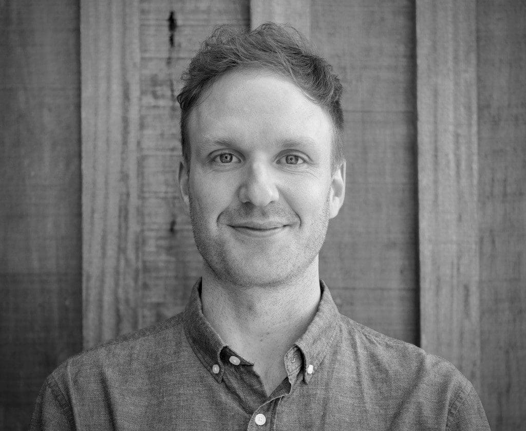 Smiling man in button-up shirt by wooden wall